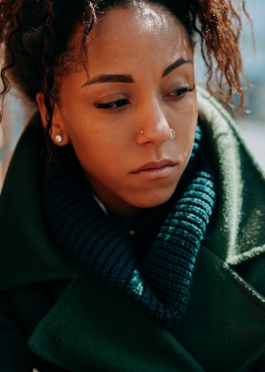 Woman in coat solemnly looks down to left.
