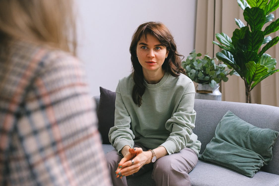 Woman sitting on a couch listening to someone talk to her.