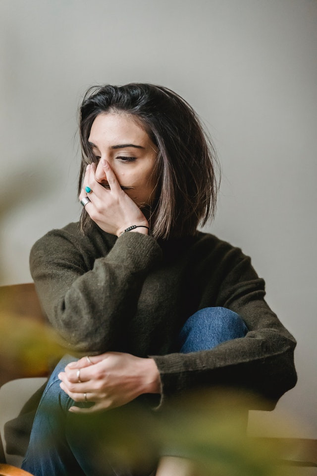 Woman sitting with one hand around her knees and the other over her mouth.