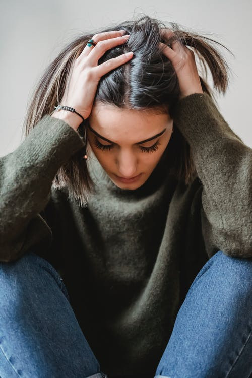 Woman holding her head with her hands while looking down.