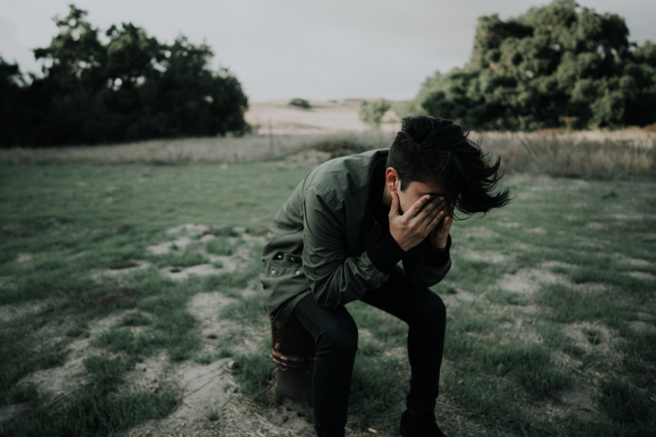 An emotional male sitting outside with his face in his hands