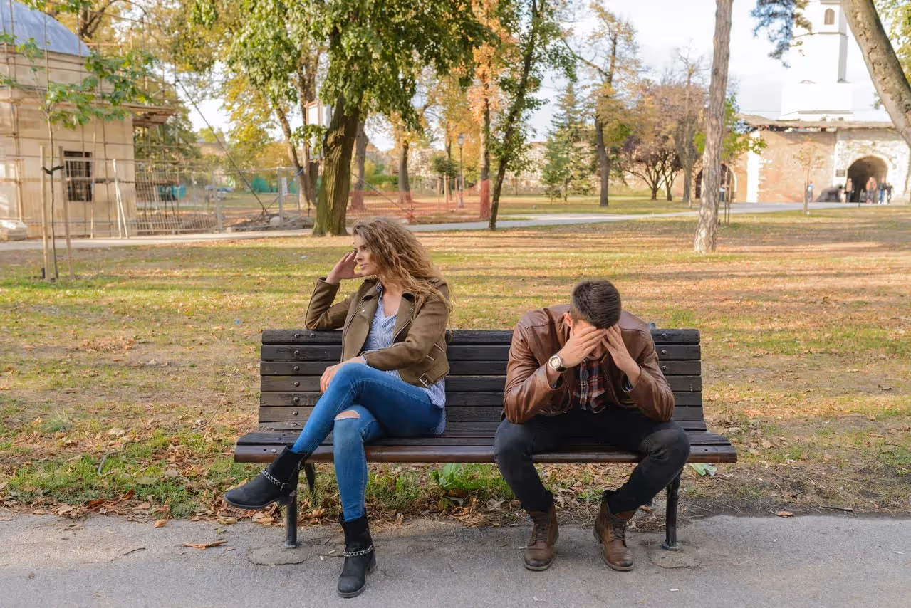 A couple sitting on a park bench not speaking or looking at eachother