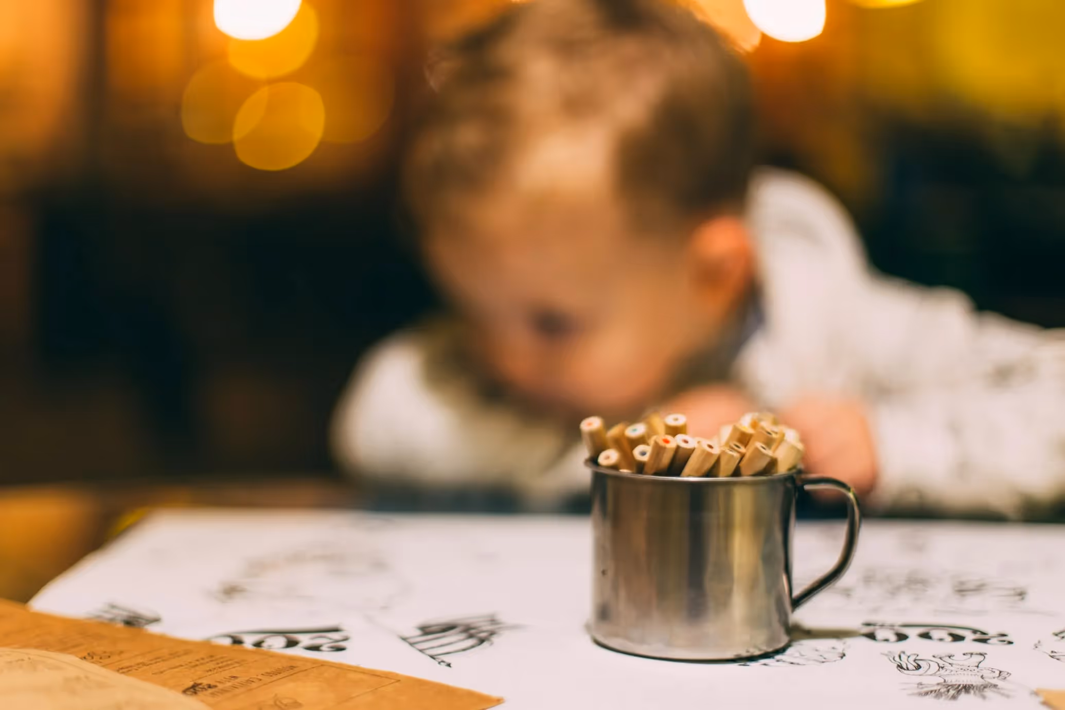 Child sitting at a table with paper and colored pencils