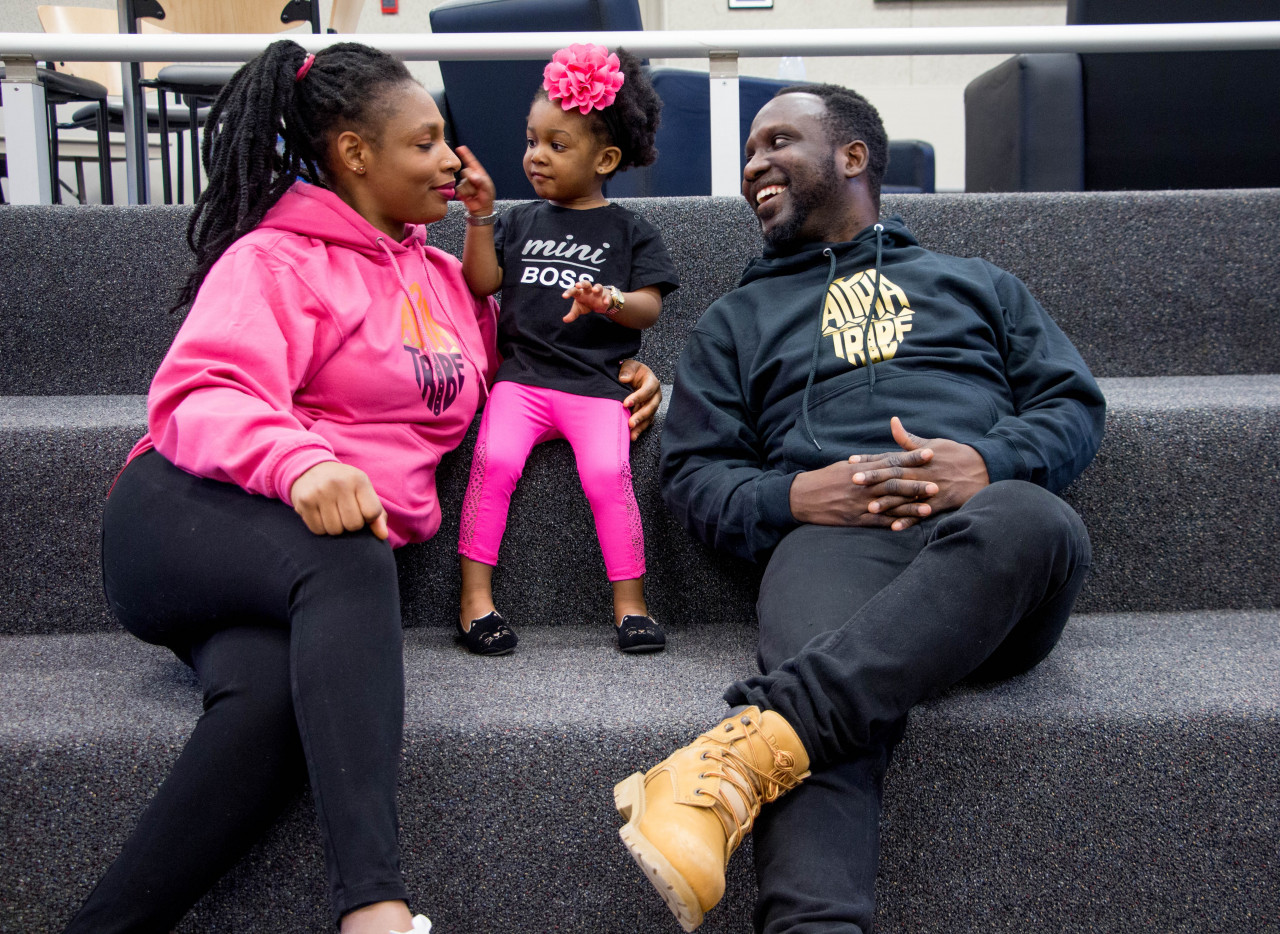 Parents sitting on steps with their young daughter between them.