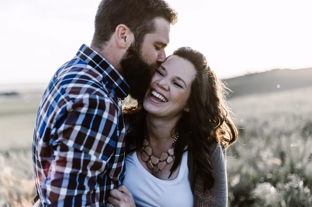 A man kissing a smiling woman in a field.