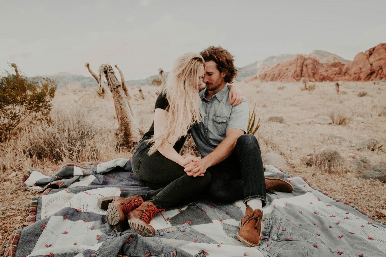Couple sitting on a blanket holding eachother.
