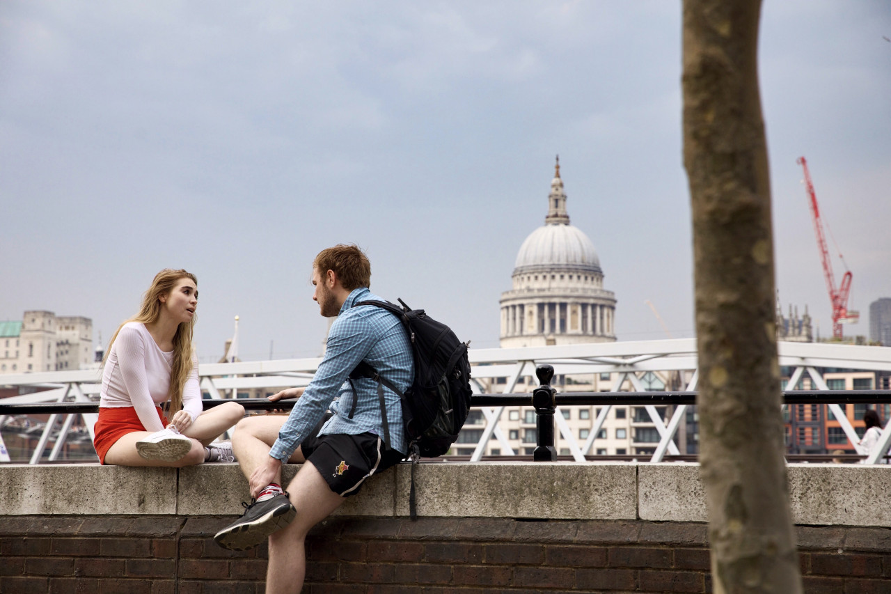 A couple sitting on the ledge of a brick wall talking.