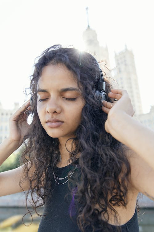 Woman standing outside holding her fingers to headphones over her ears.