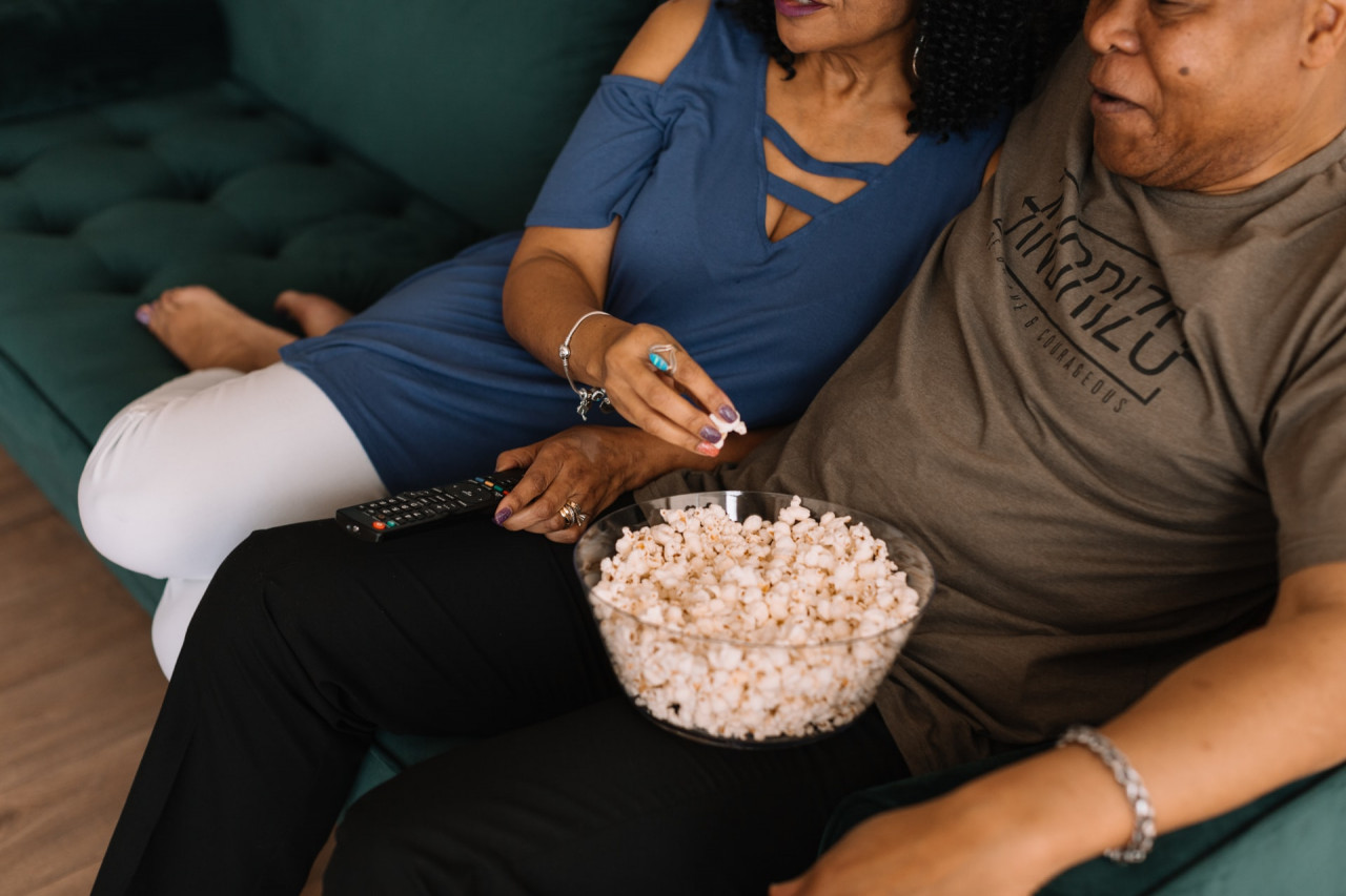 Couple sitting on the couch watching a movie and eating popcorn