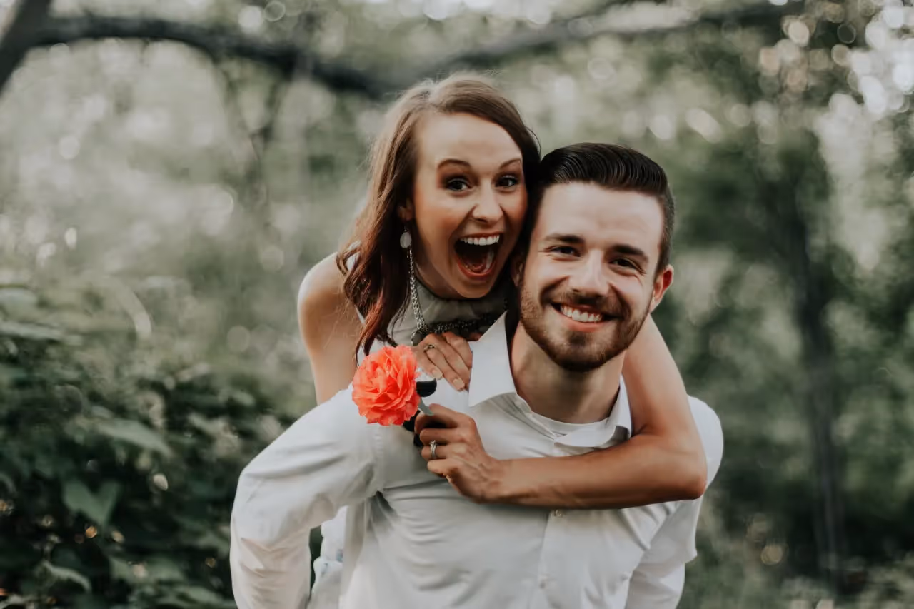 A man smiling with a woman smiling on his back.