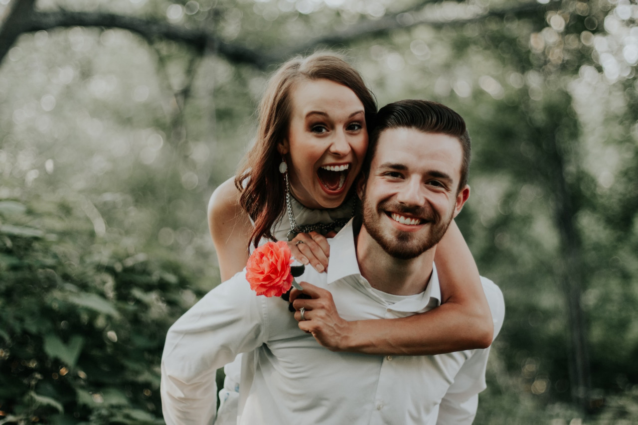 A man smiling with a woman smiling on his back.