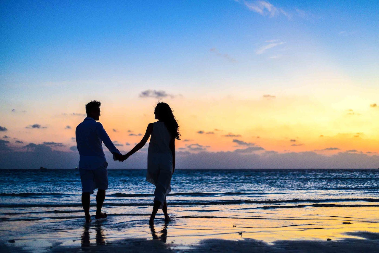 A couple holding hands and walking on the beach at sunset