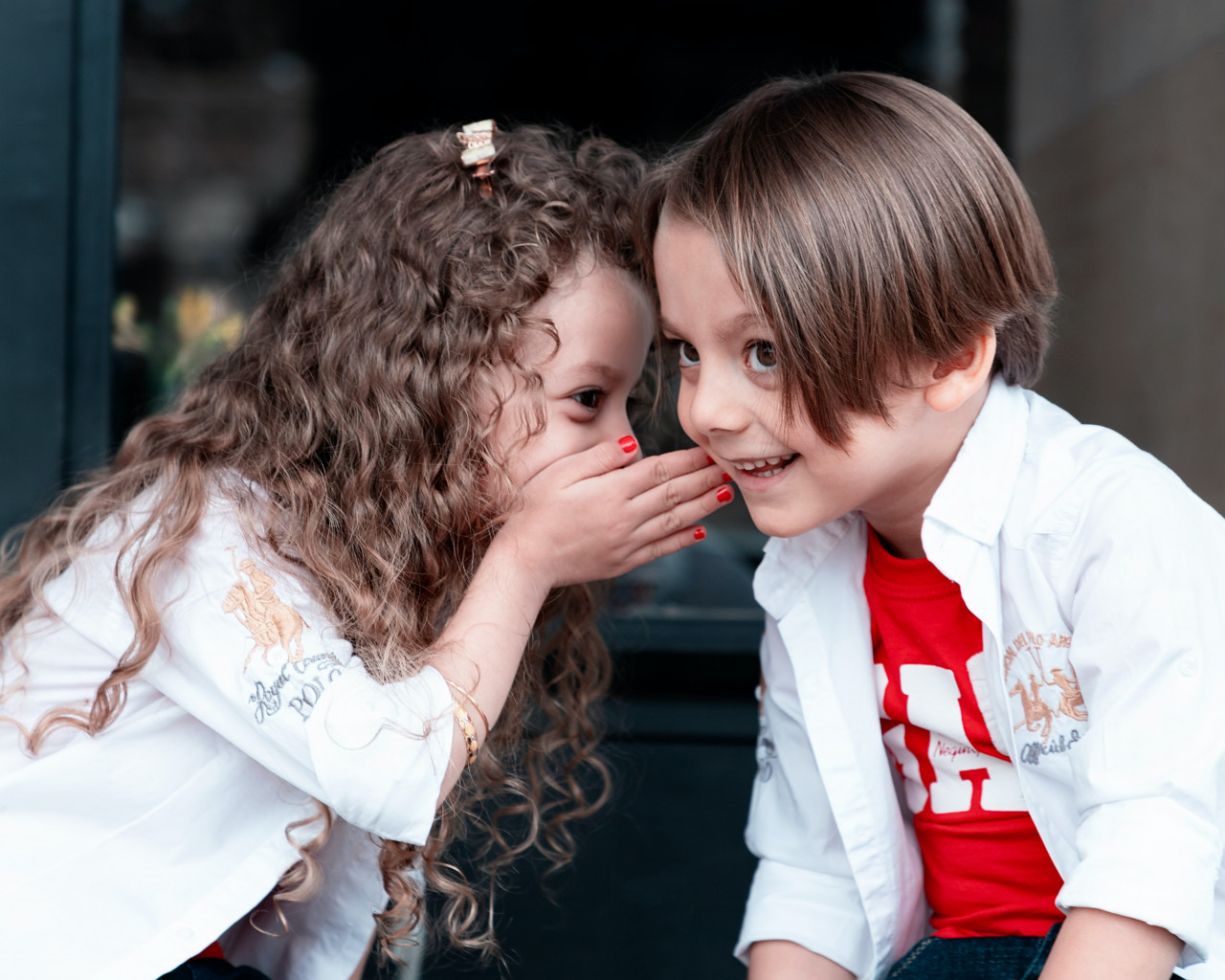 A little girl whispering something to a little boy.