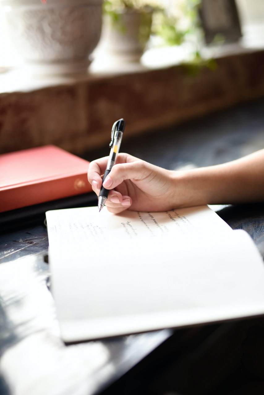 A person writing on a notebook outside.