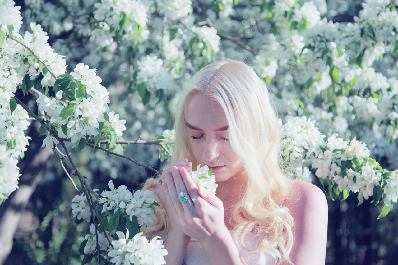 Blonde woman smelling flowers from a tree