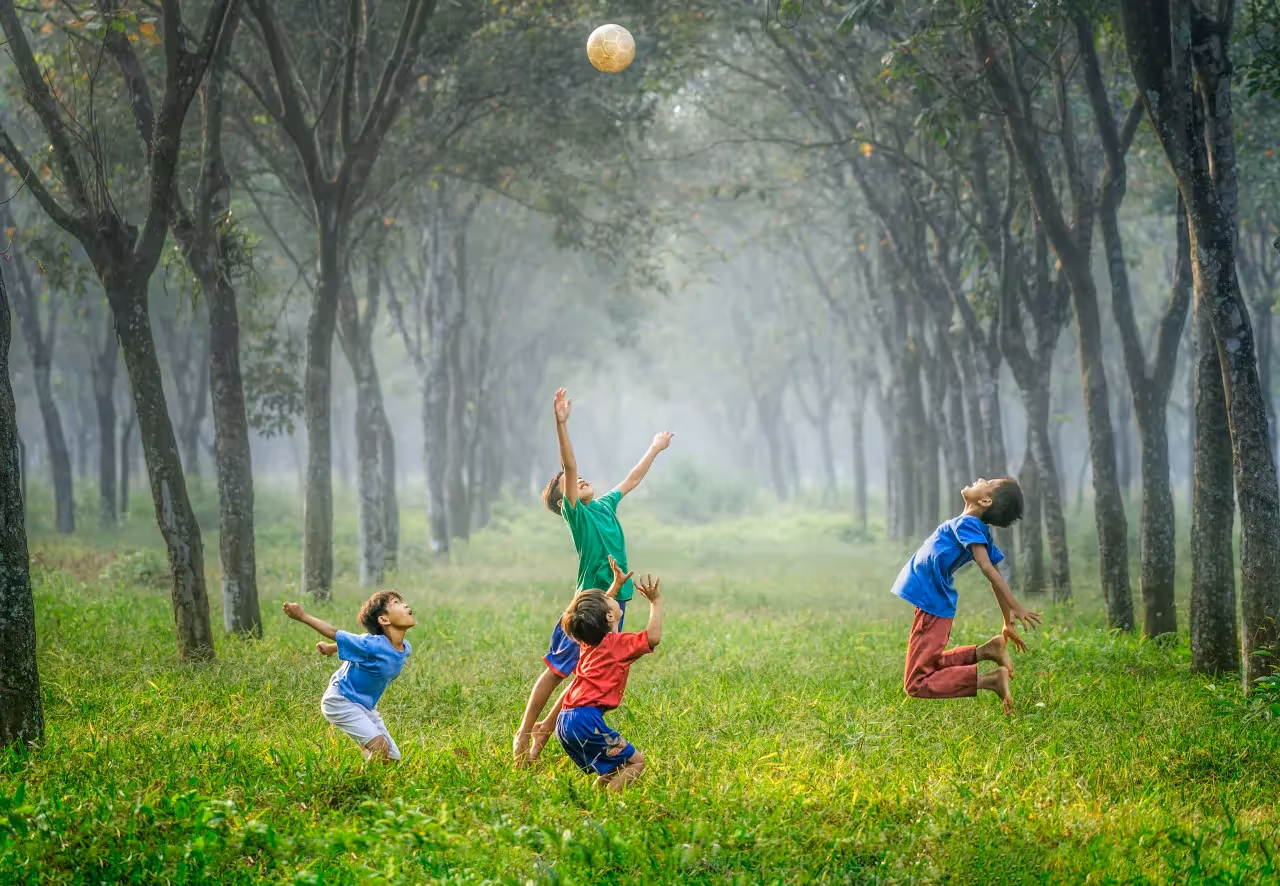 A group of boys throwing a soccer ball in the air in a grassy area