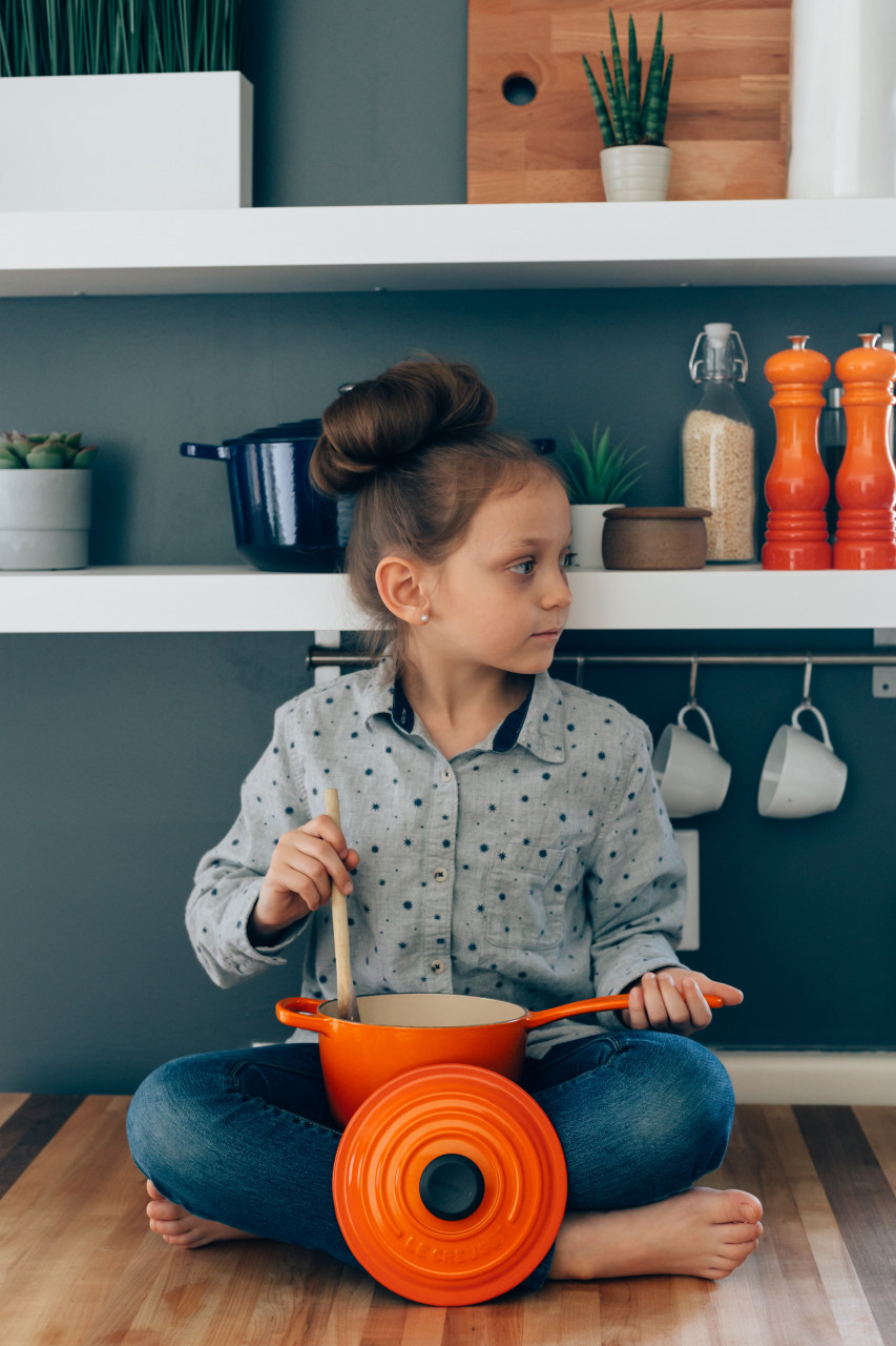 A child sitting on the floor stirring a wooden spoon in a pot on her lap