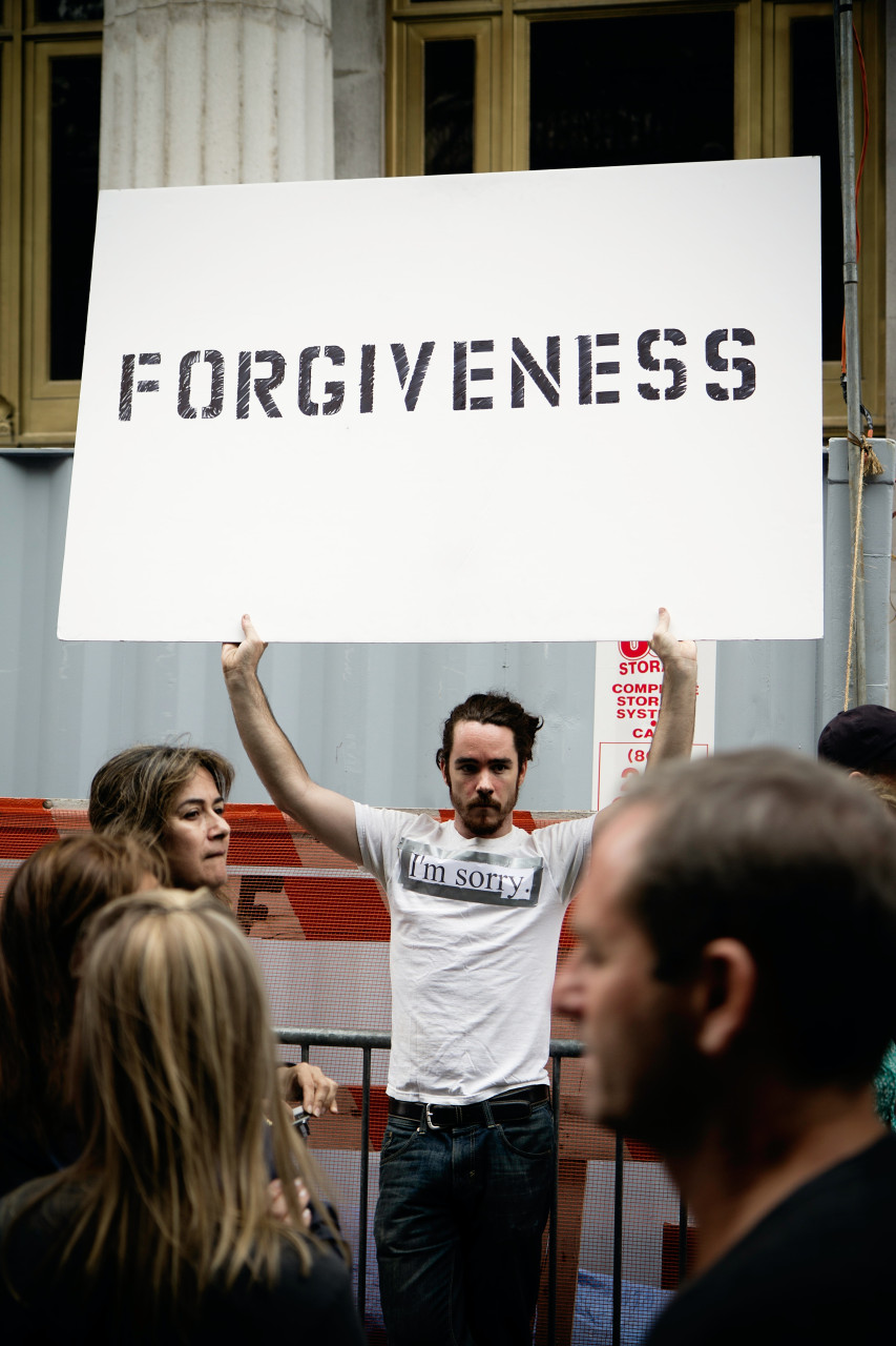 A man holding up a board of forgiveness in public.