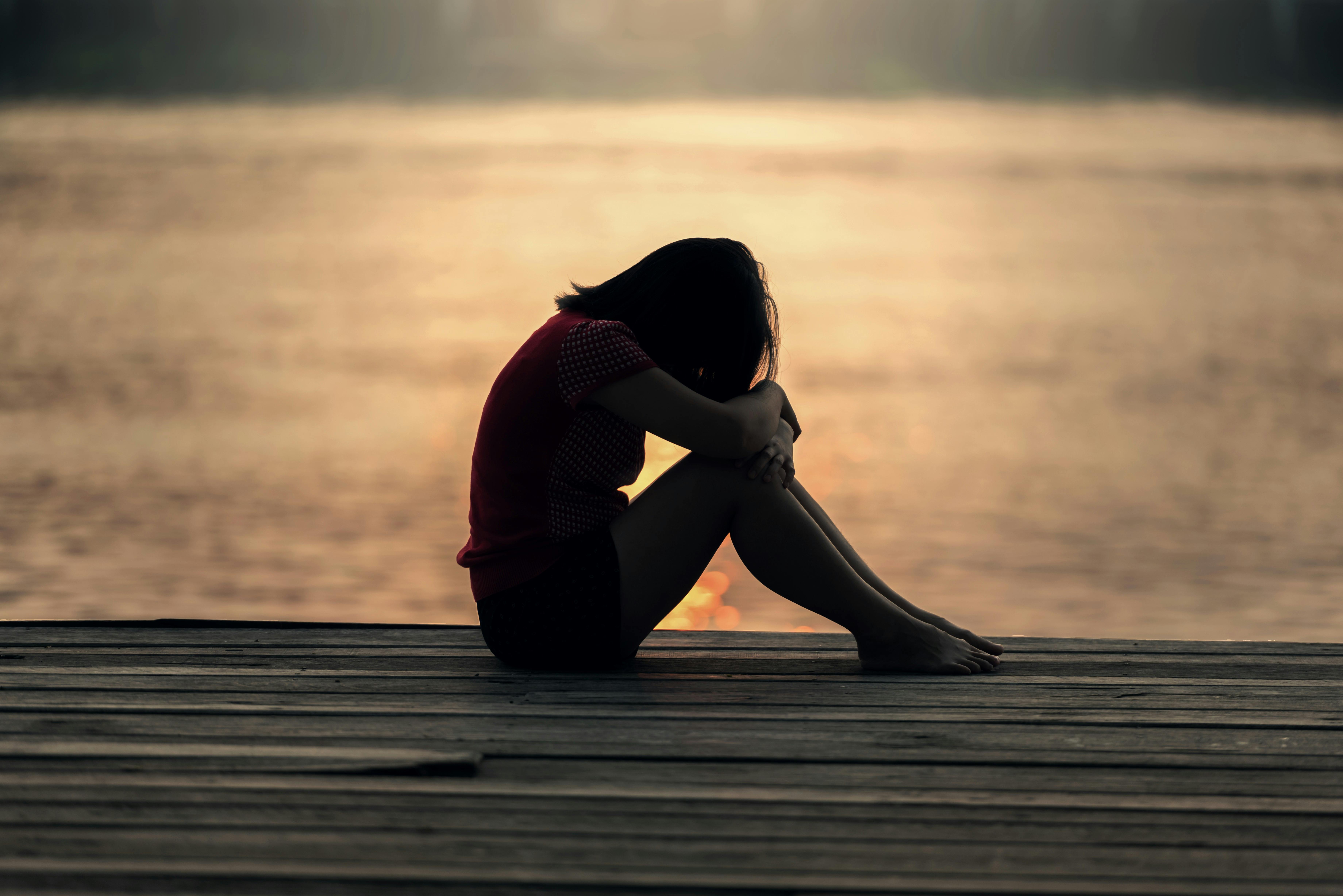 Child sitting down on a dock by the water with her head on her knees