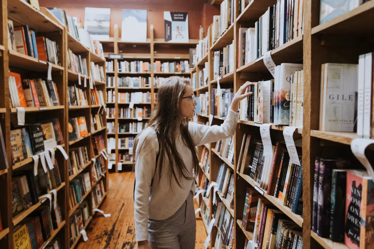 A teacher in the library looking at books on the shelf.