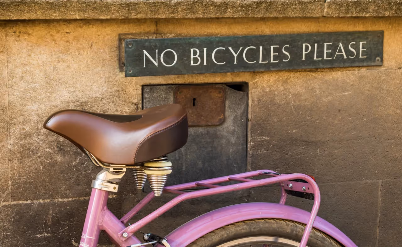 A pink bike is parked next to a sign that says no bicycles, please.