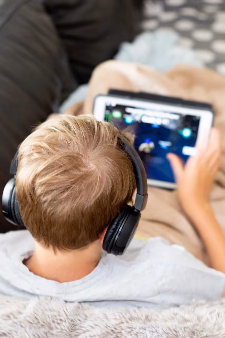 A child wearing headphones play on a tablet.
