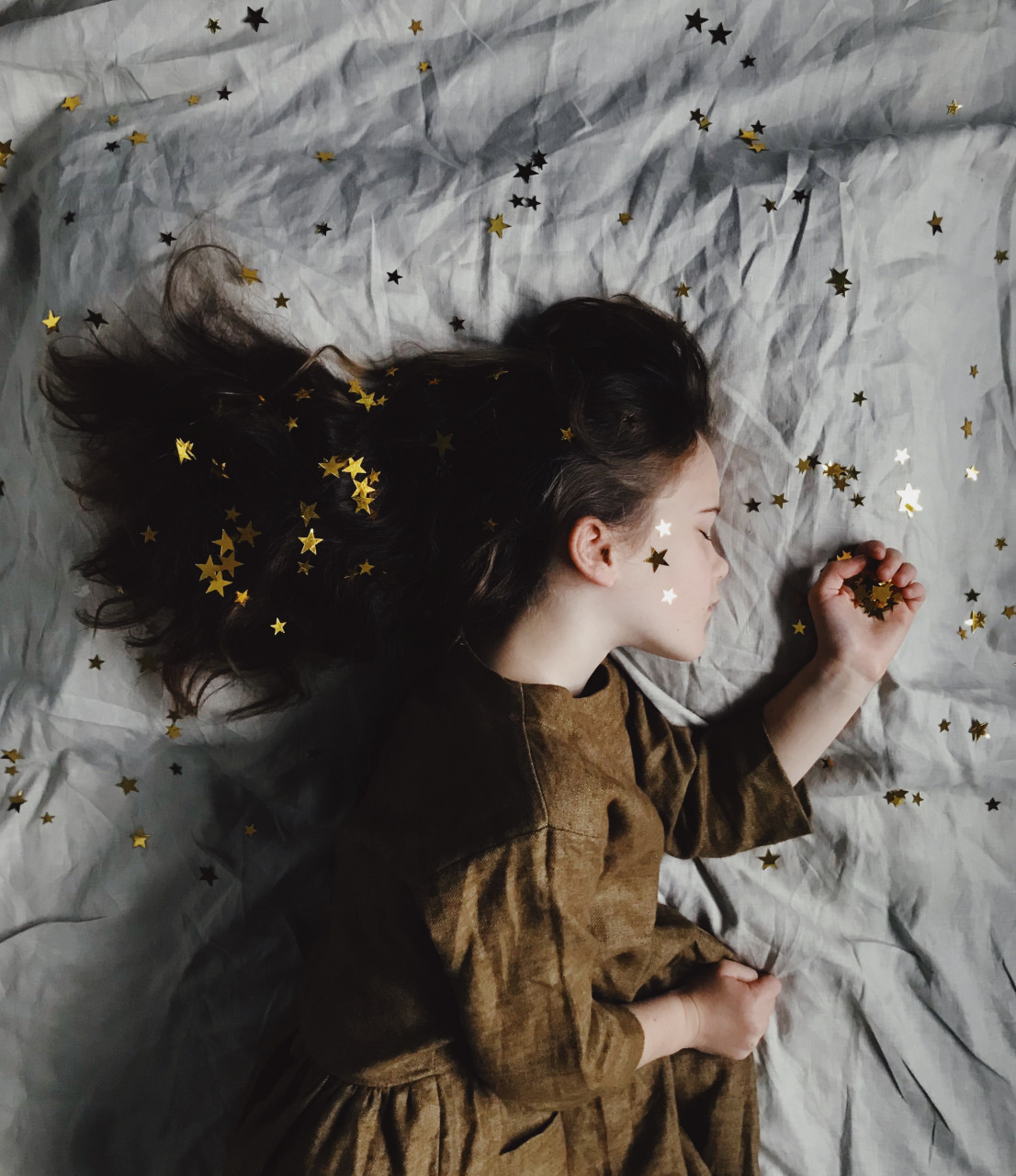 A little girl sleeping on a white shit with gold stars spread around