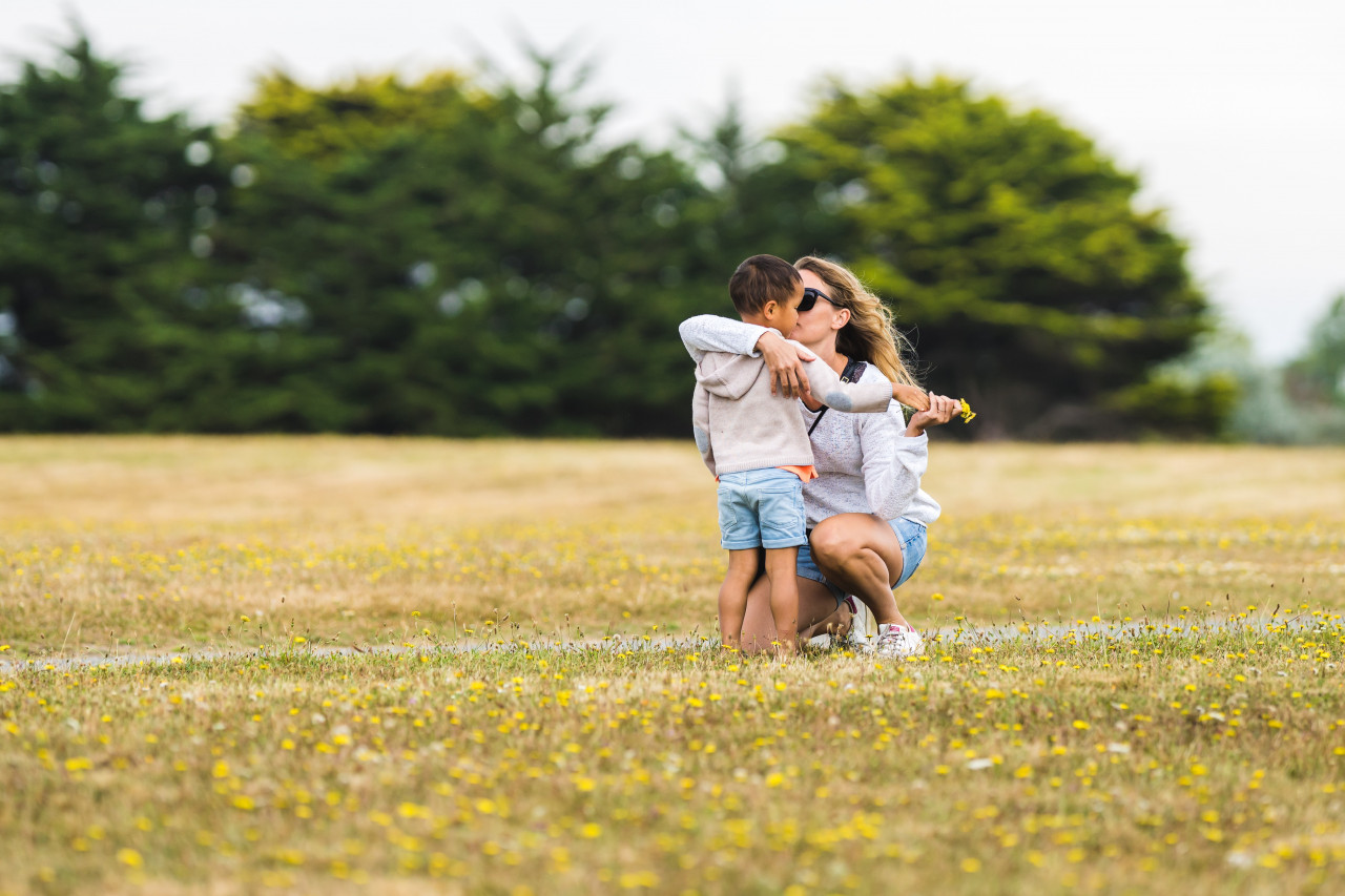 Woman with her arm wrapped around a child in a field of dandelions.