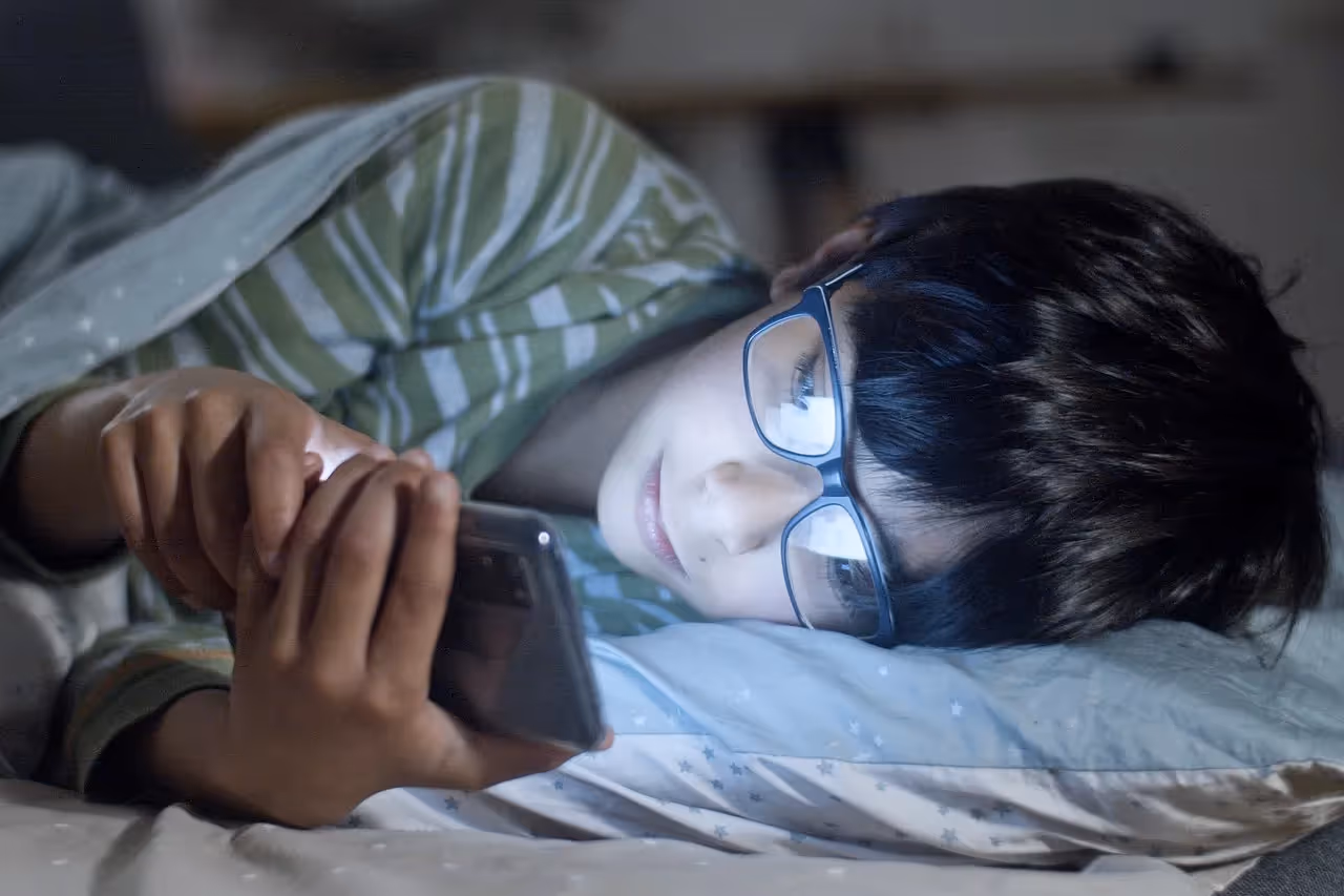child laying in bed playing on phone