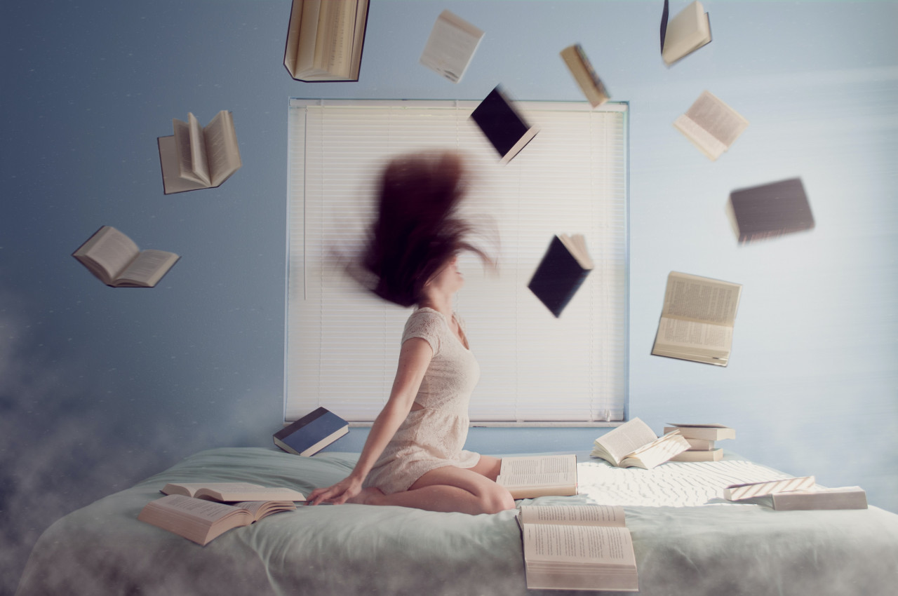 A girl on a bed with books falling around around