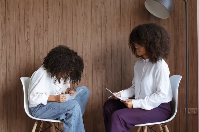 Two females sitting in chairs with pen and paper