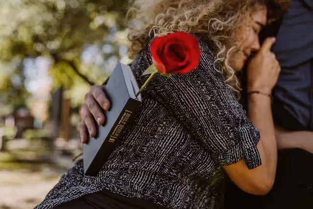 A woman crying and leaning on someone holding a rose and bible