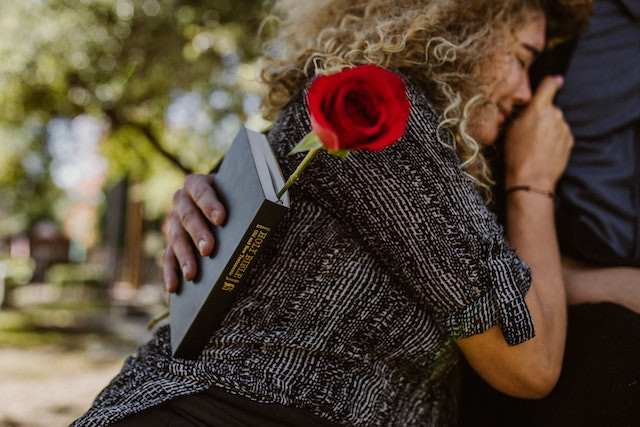 A woman crying and leaning on someone holding a rose and bible