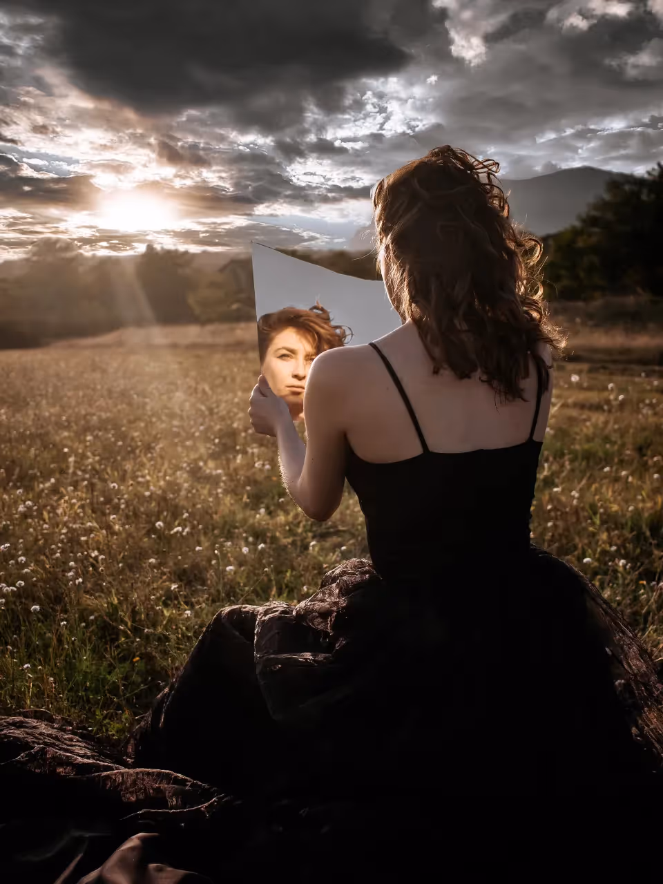 Woman sitting in a field looking at herself in a mirror
