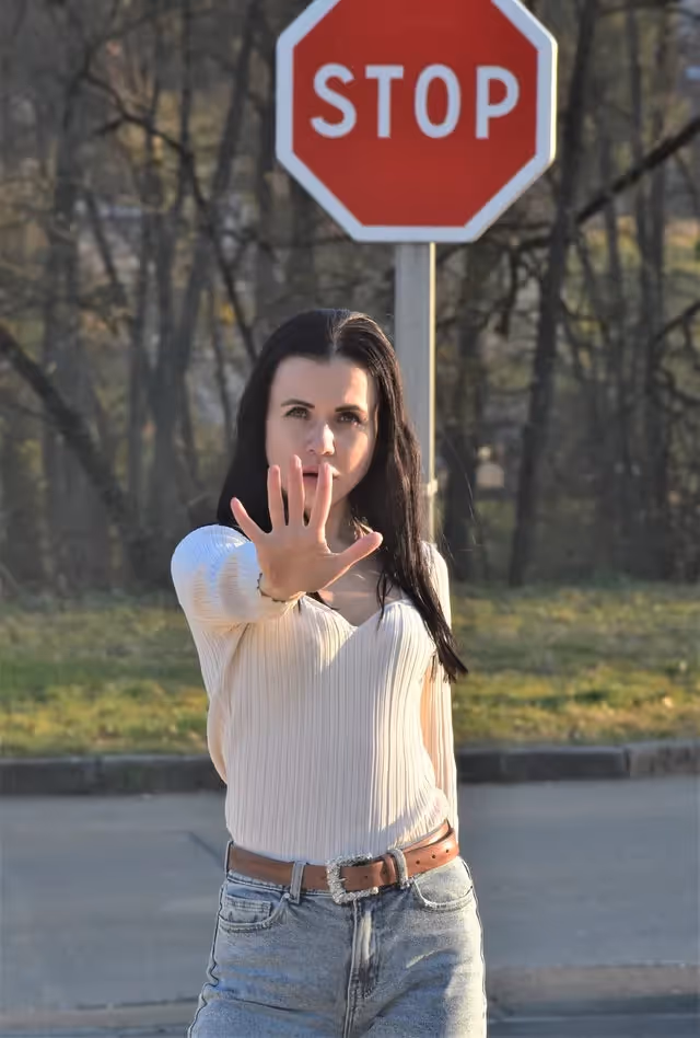 Woman standing in front of a stop sign with her hand out to stop