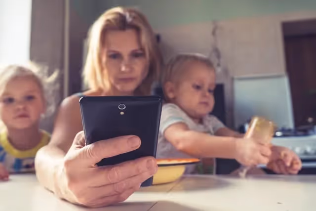 Mom sitting at a table with her 2 young children looking at her phone