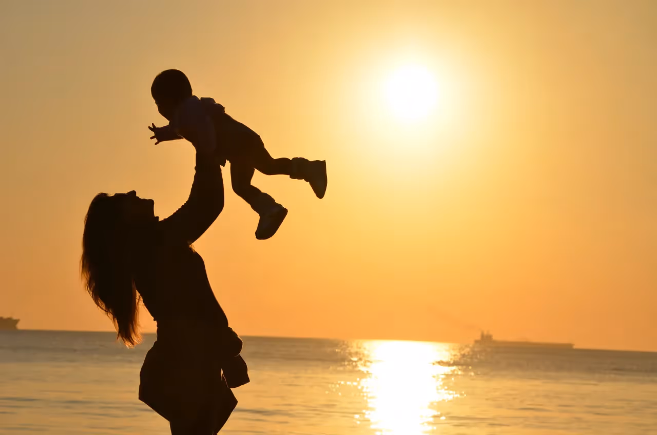 A mother holding her baby in the air during sunset