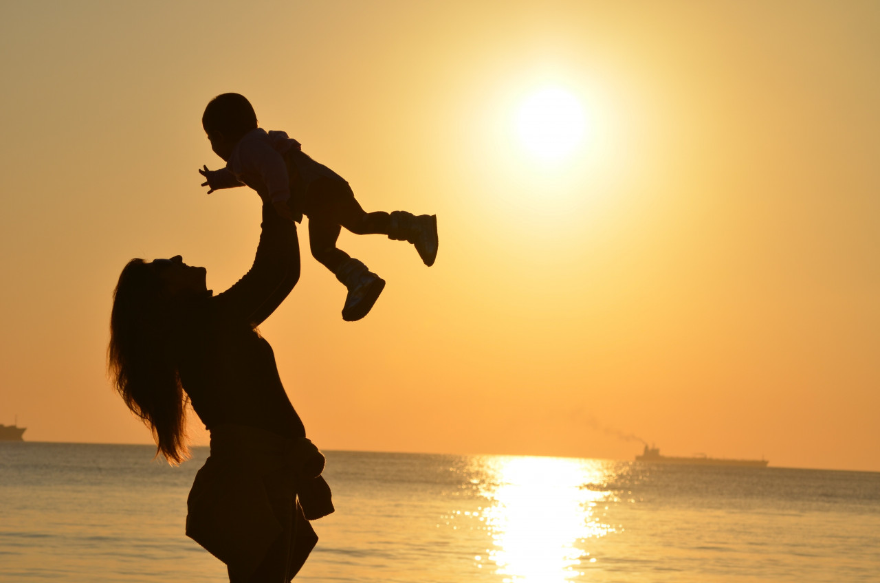 A mother holding her baby in the air during sunset
