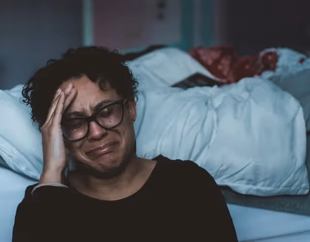 A woman sitting next to her bed crying