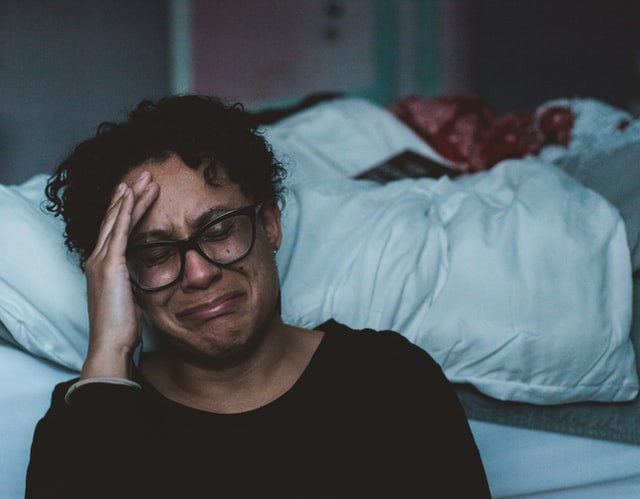 A woman sitting next to her bed crying