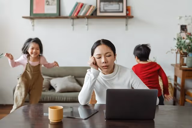 Mom sitting at her computer while her kids play in the background