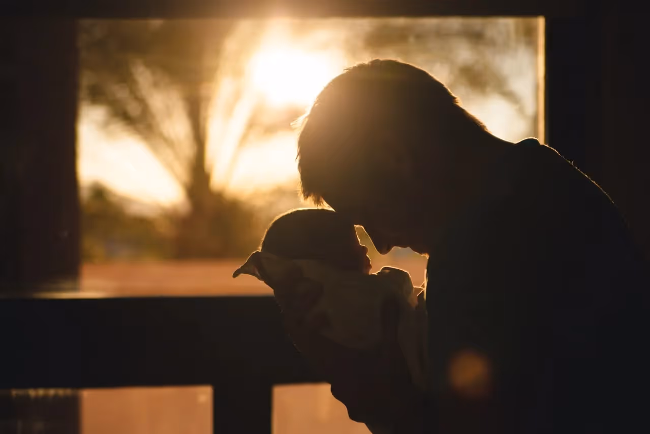 Man standing in front of a window touching his head to his baby's head