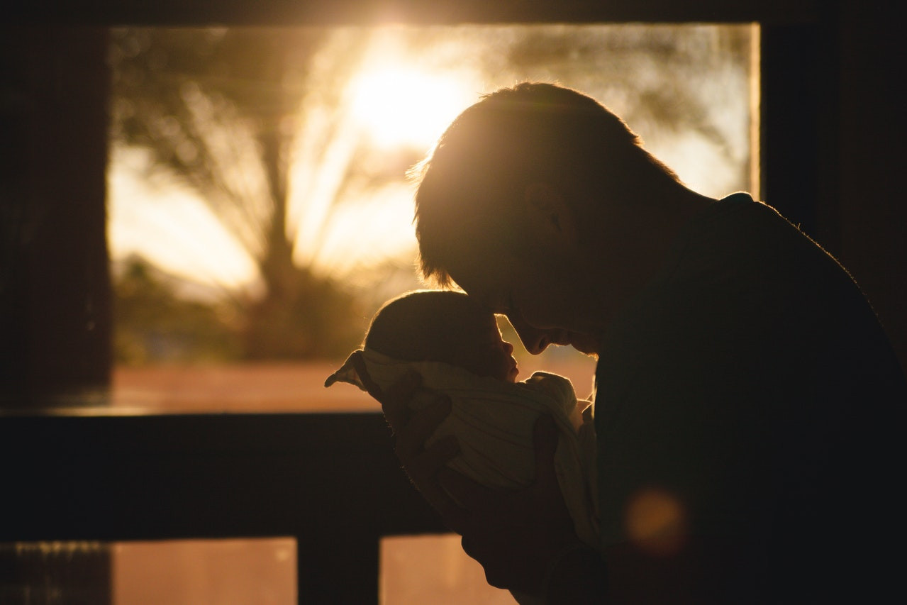 Man standing in front of a window touching his head to his baby's head
