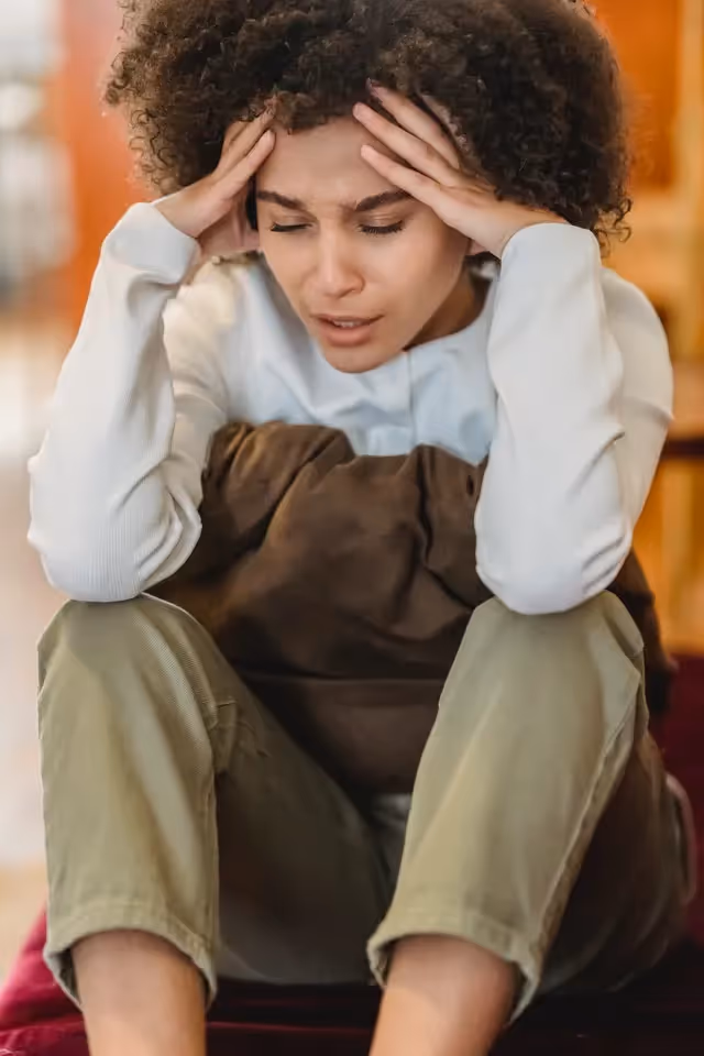 Woman sitting on the floor with her hands on her head.