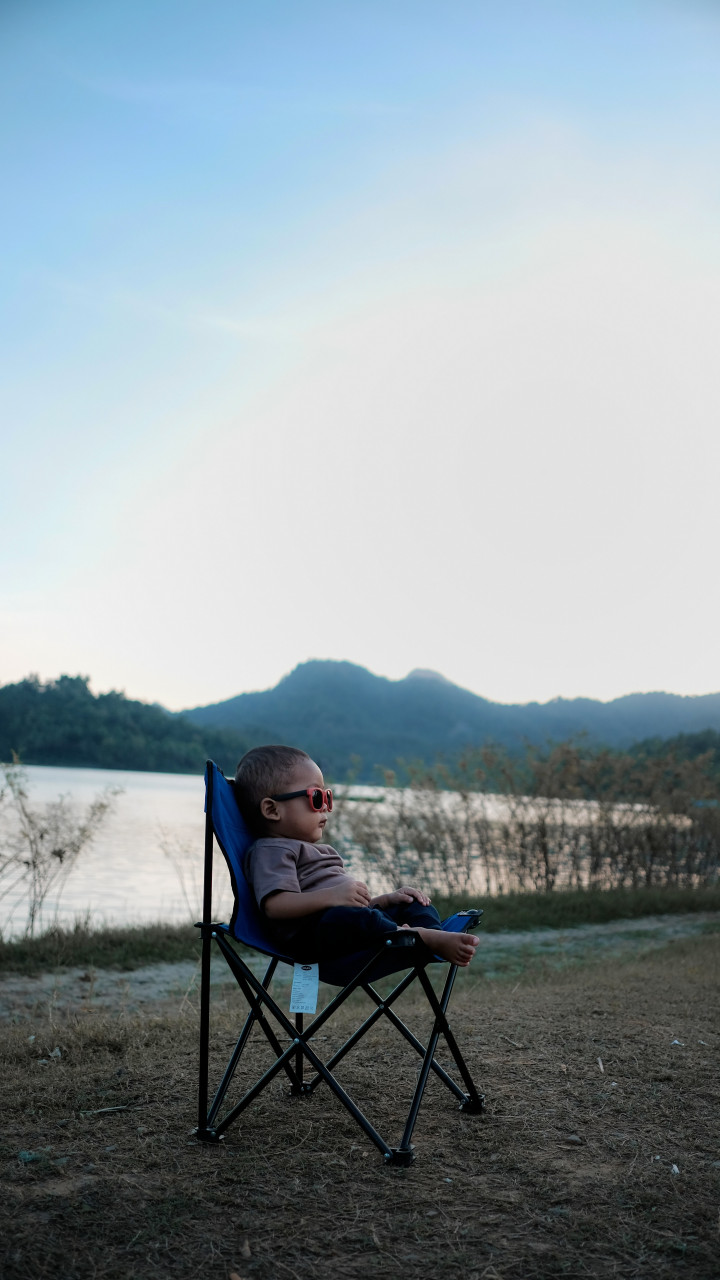 A boy lounging on a chair outdoors.