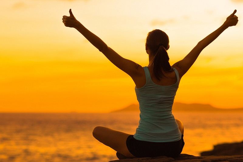 A woman overlooking the water with her arms raised in the air giving thumbs up