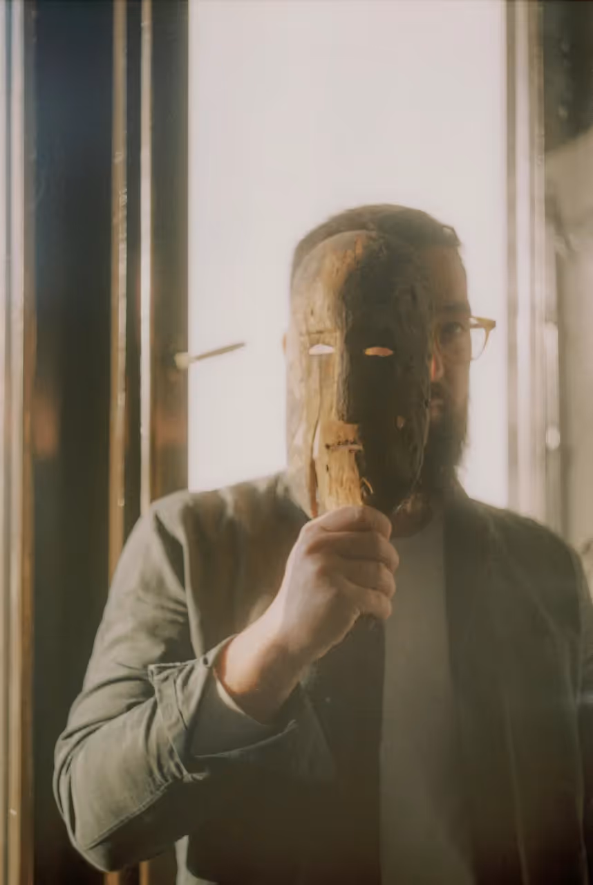 Man holding a wooden mask over part of his face