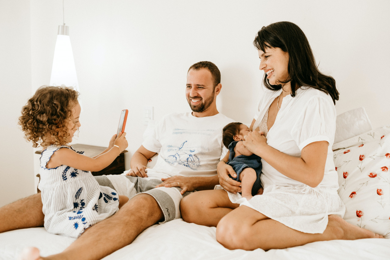 A mom and dad sitting in bed with their young children.