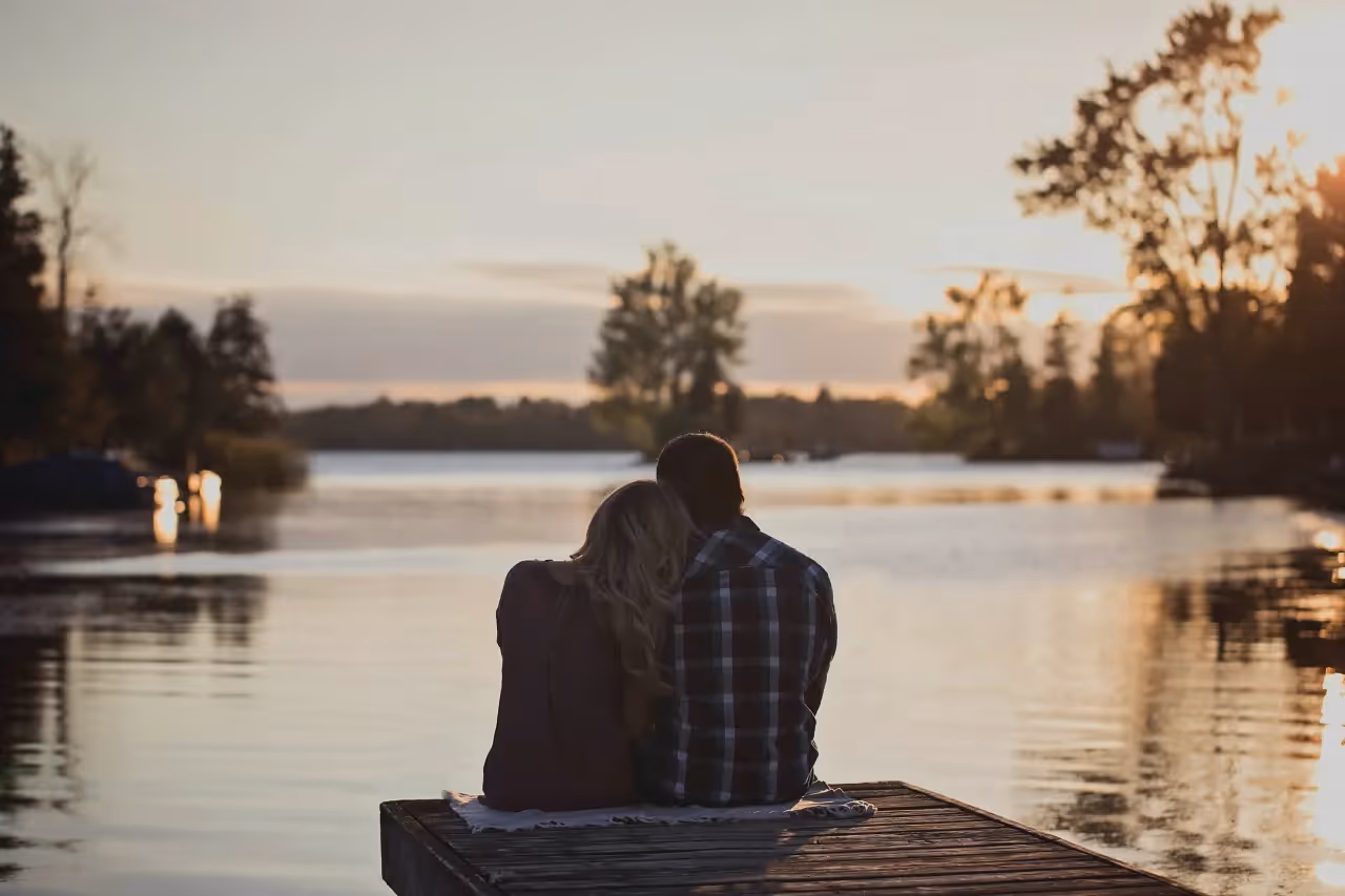 two people sitting on the edge of a dock overlooking the water