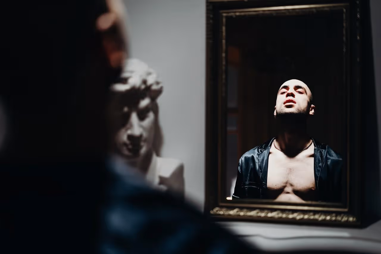 Man with his shirt undone staring at himself in the mirror